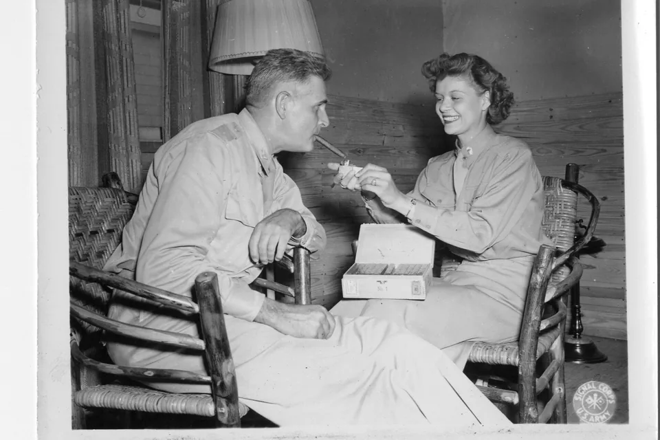 Hemingway Short Story Cigar Review — historic 1943 photograph of a woman lighting a cigar for a seated officer