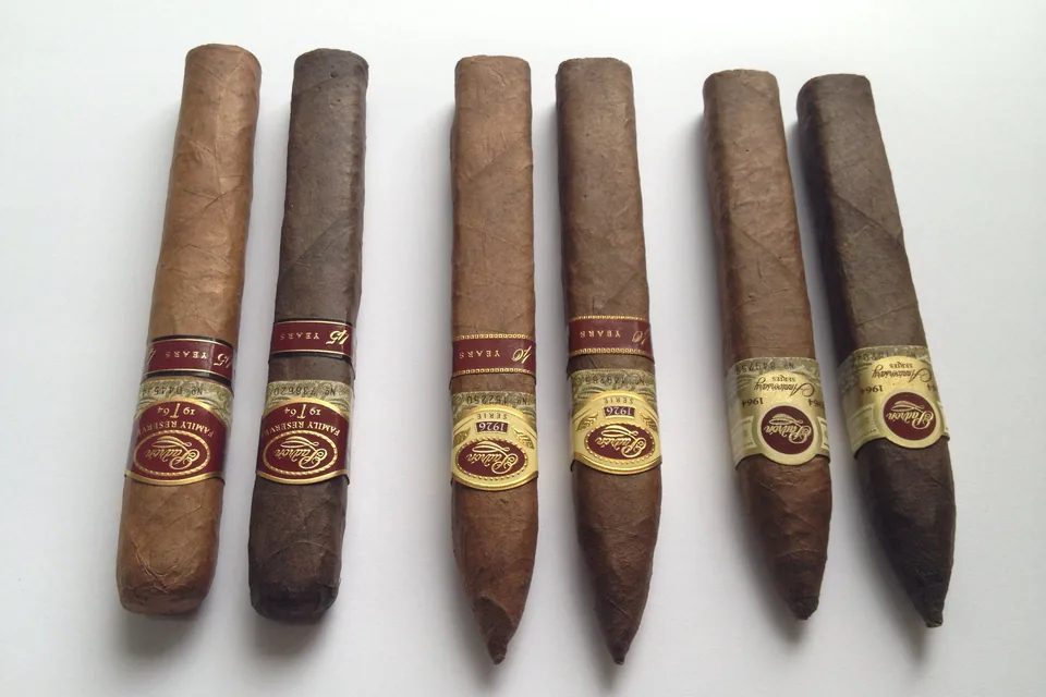 Six cigars of different shapes and shades standing upright in a row