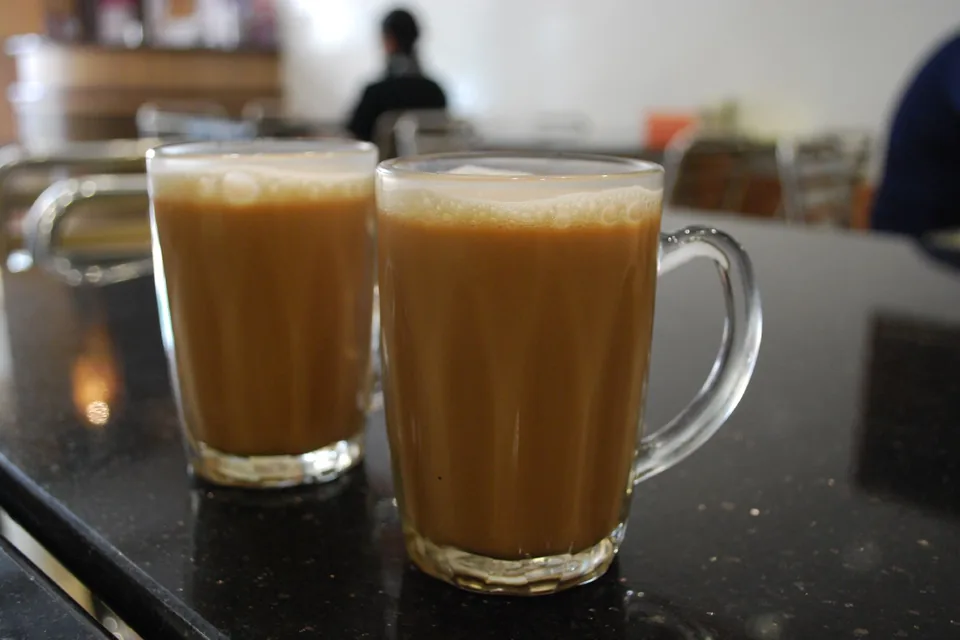 Two glass mugs of frothy teh tarik on a dark table in a Malaysian eatery