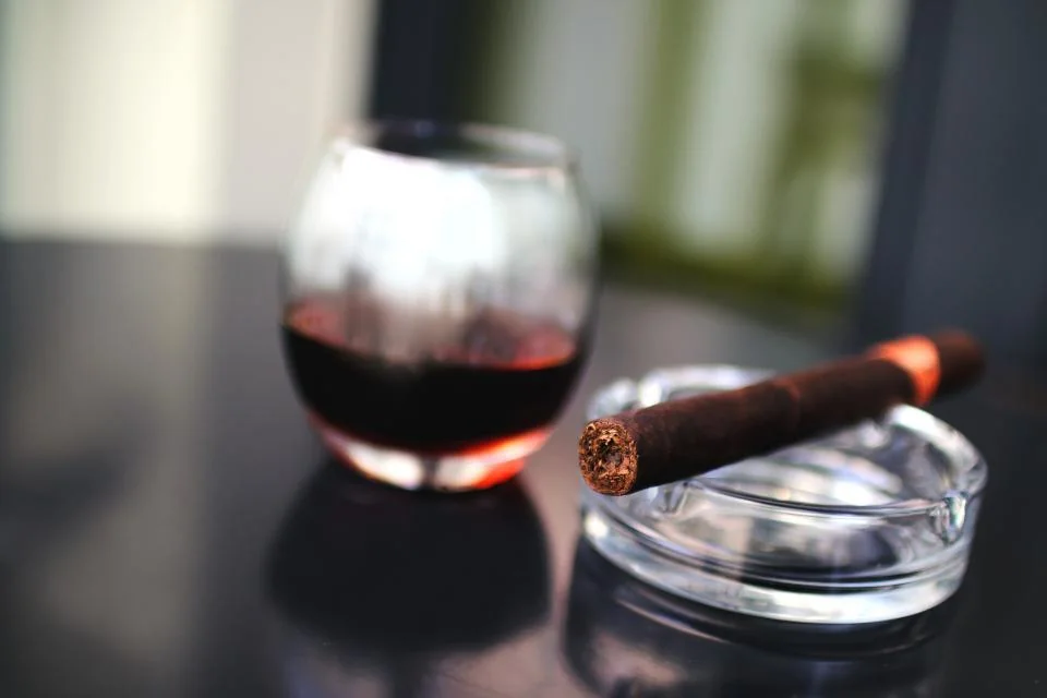 Types of Cigars: A Complete Guide to Shapes, Sizes and Styles — unbranded cigar resting on a glass ashtray beside a glass of red wine on a dark table