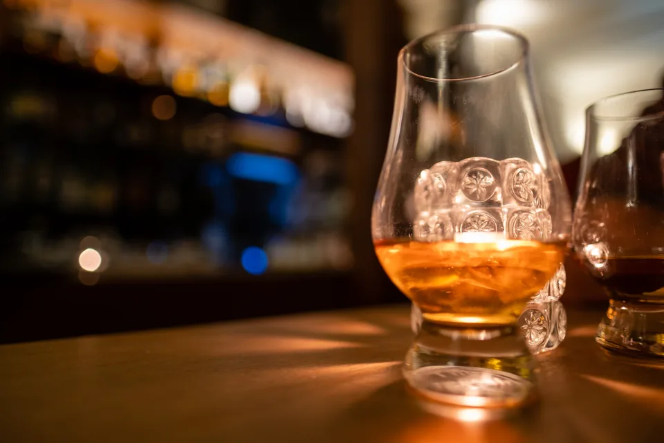 Romeo y Julieta Churchill Review — nosing glass of amber whisky on a dark bar with warm bottles behind